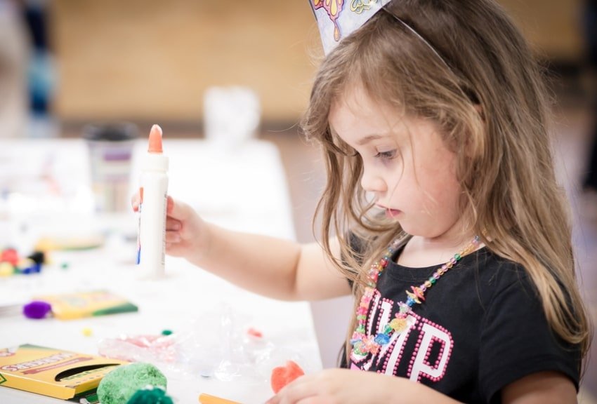 Bambino al tavolo delle arti e mestieri con in mano una colla